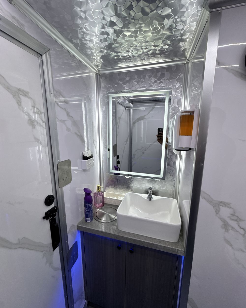 The vanity: a white vessel sink on a stone counter beneath a back-lit mirror, with accent lighting along the cabinet.